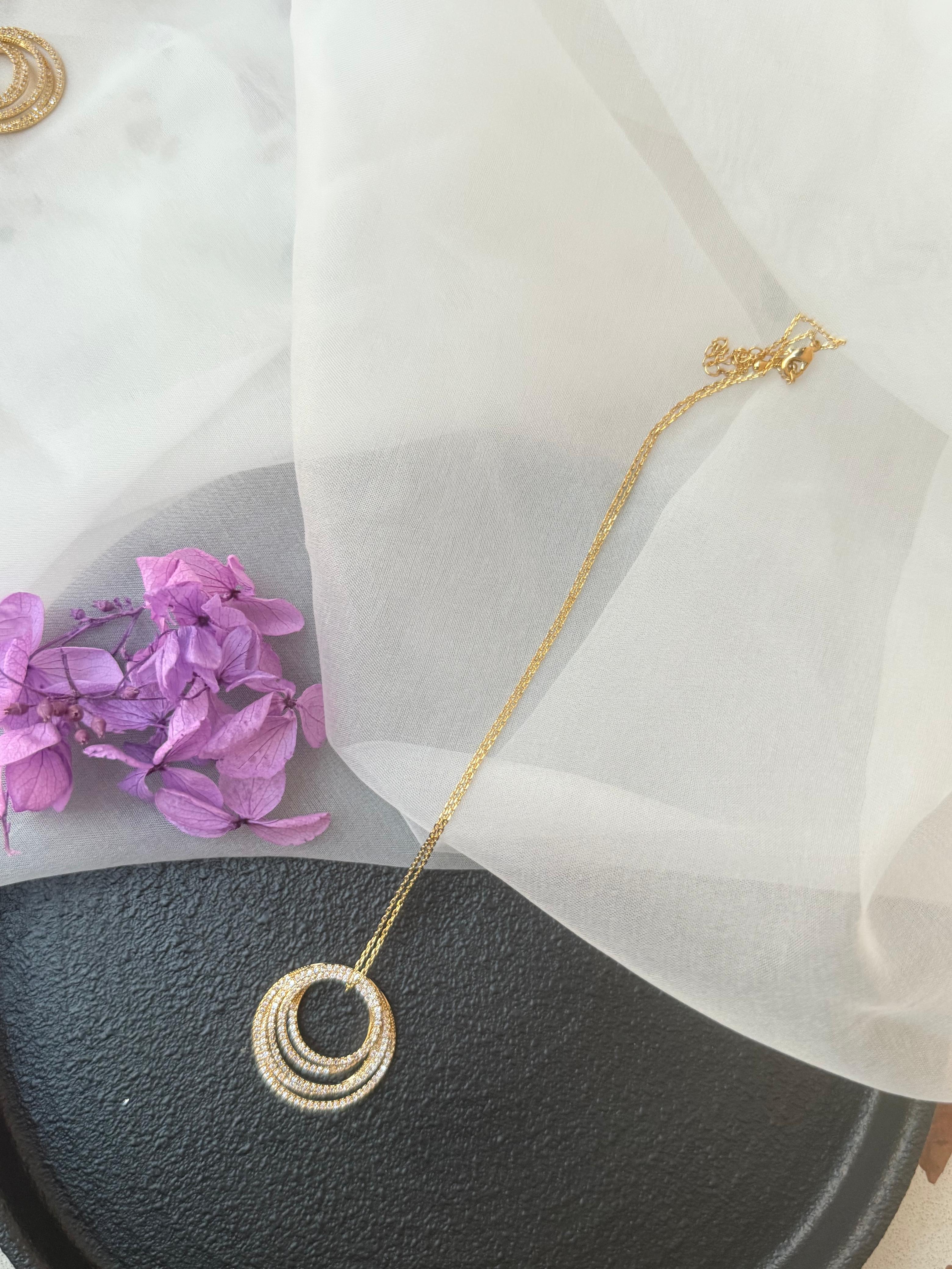 Eva Gold Pendant triple concentric circle diamond charm on a fine gold chain displayed on white tulle with purple dried flowers